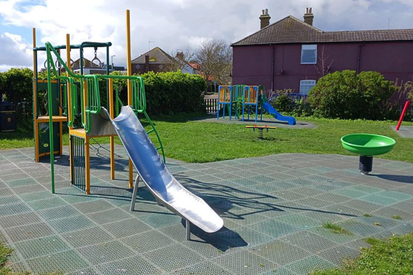 A picture of a climbing frame with a metal slide. A spin bowl, seesaw and second climbing frame can also be seen