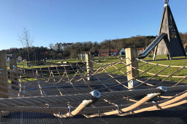 A photo of climbing equipment. the equipment has wooden posts with a net spread between them