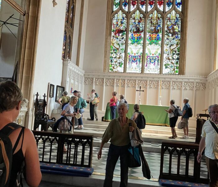 People are milling around a church. A large stained-glass window is at the far end