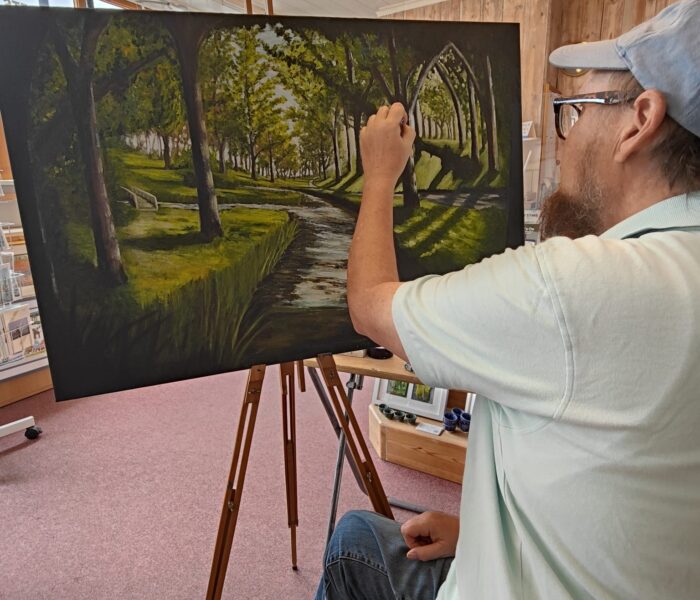 A person is painting a picture. It is a forest scene with a path running through the middle