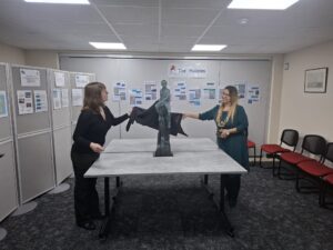 Two people stand either side of a small statue, removing a black cloth
