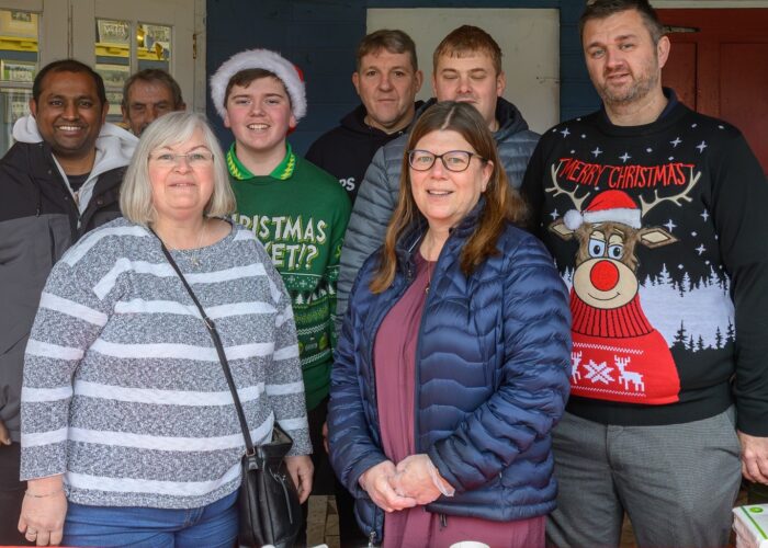 A group of people stand behind a table serving hot drinks