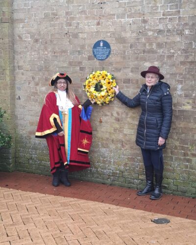 Image of two people standing beside a hanging commemorative wreath