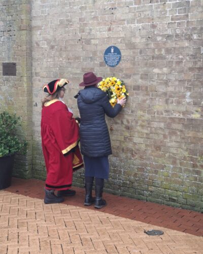 Image of two people hanging a yellow commemorative wreath on a wall