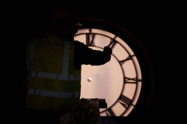 The silhouette of a person working on the illuminated clock face