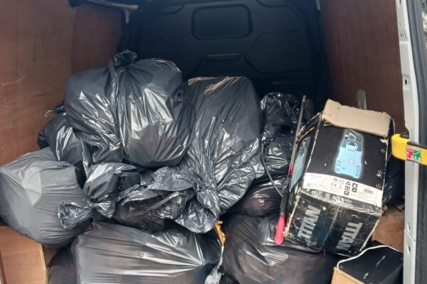 A photo of a large number of filled black bin bags in the back of a van.